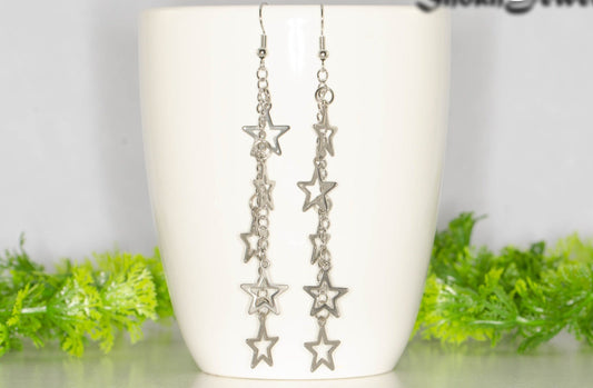 Long stainless steel chain and star earrings on a coffee mug.
