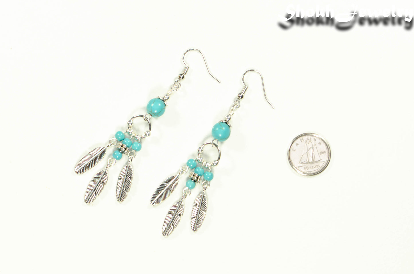 Statement Turquoise Howlite And Feather Earrings beside a dime.