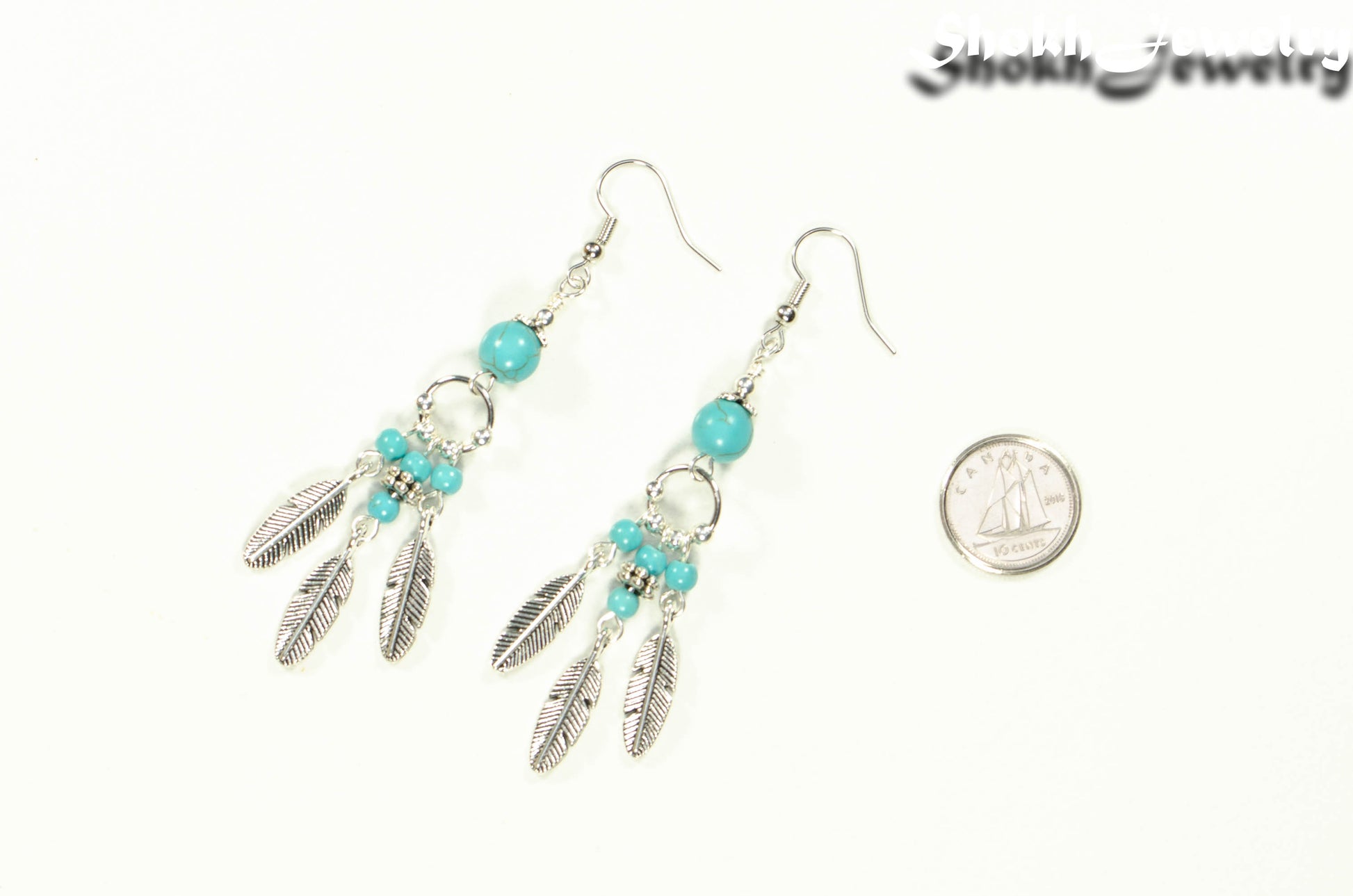 Statement Turquoise Howlite And Feather Earrings beside a dime.