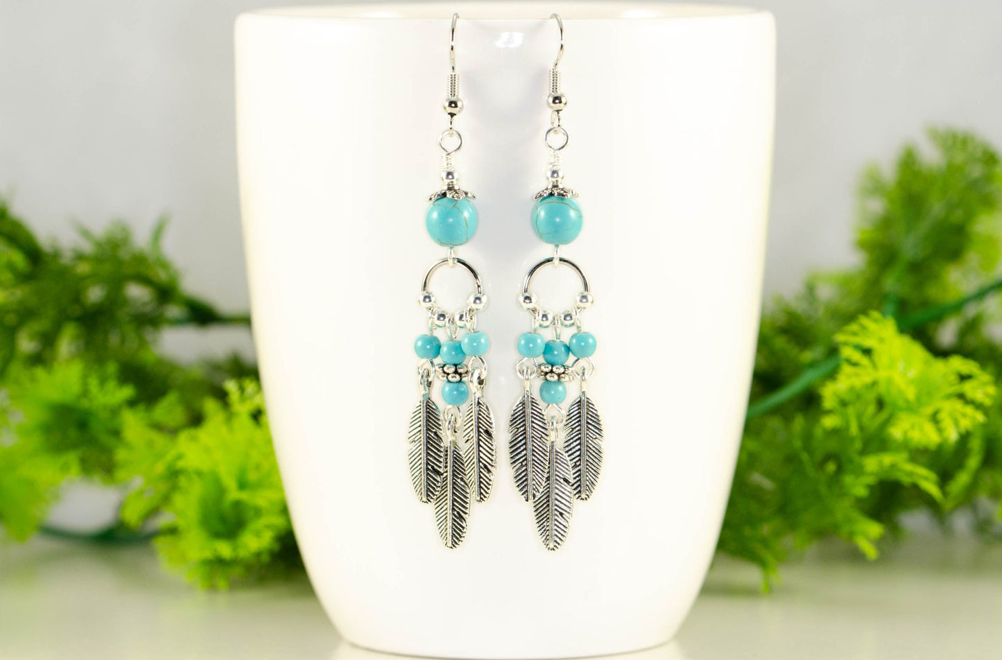 Statement Turquoise Howlite And Feather Earrings displayed on a coffee mug.